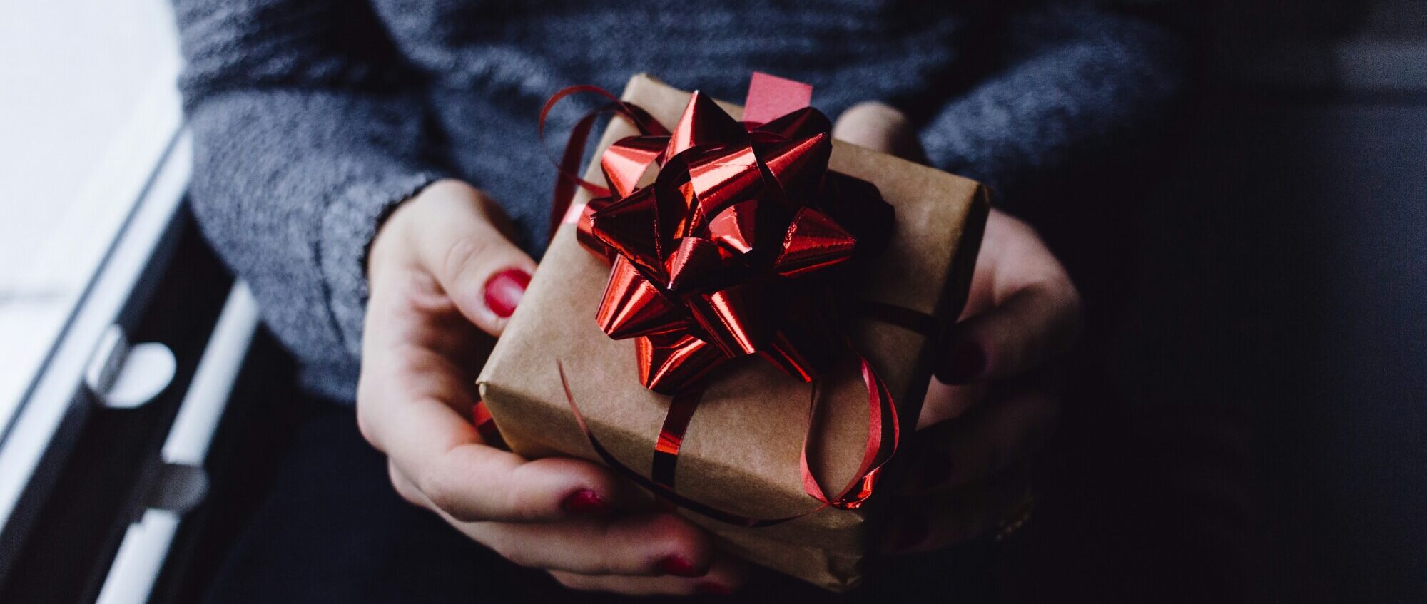 Es ist ein Geschenk mit einer Schleife zu sehen, welches eine Person in der Hand hält.