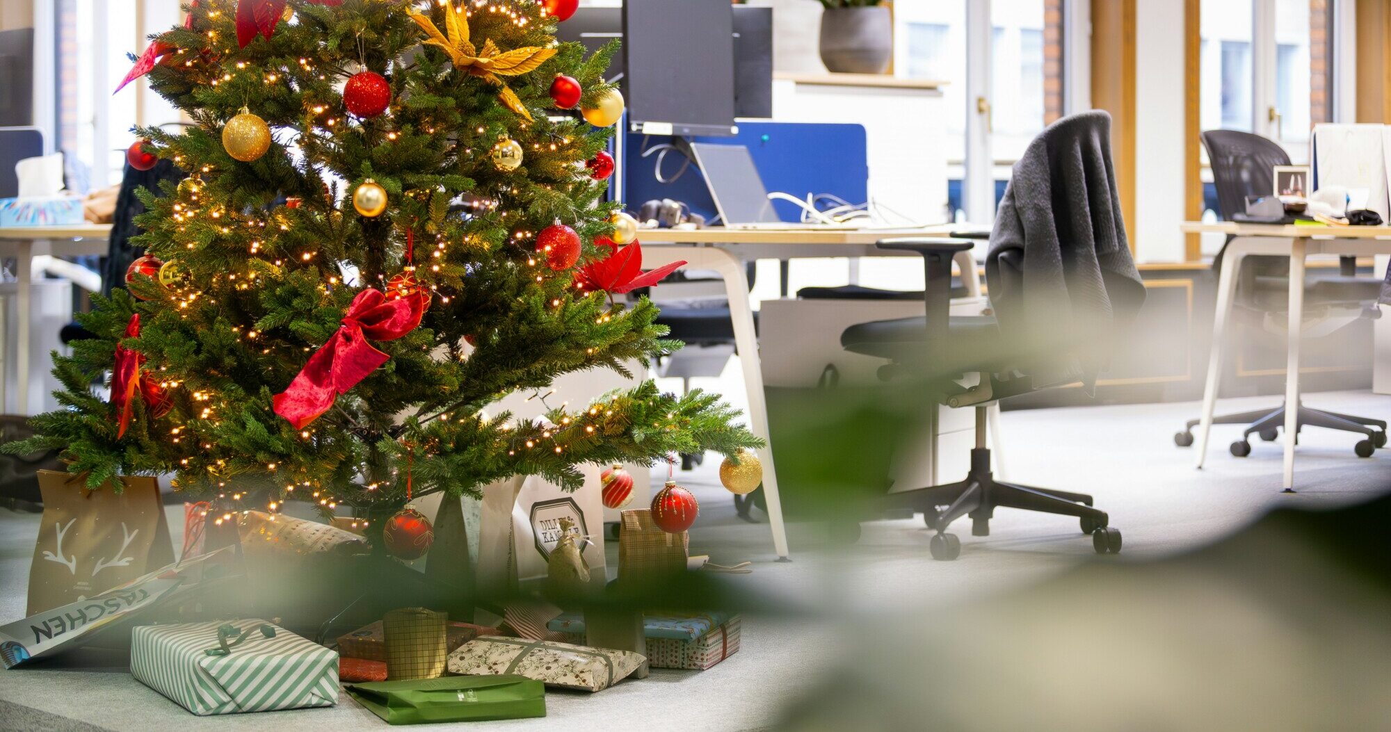 Ein geschmückter Weihnachtsbaum mit Geschenken steht in einem Büro.