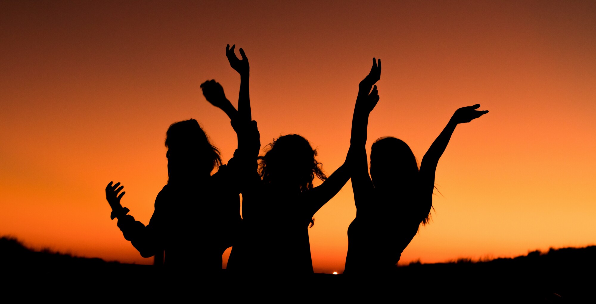 drei Frauensilhouetten tanzen im Sonnenuntergang