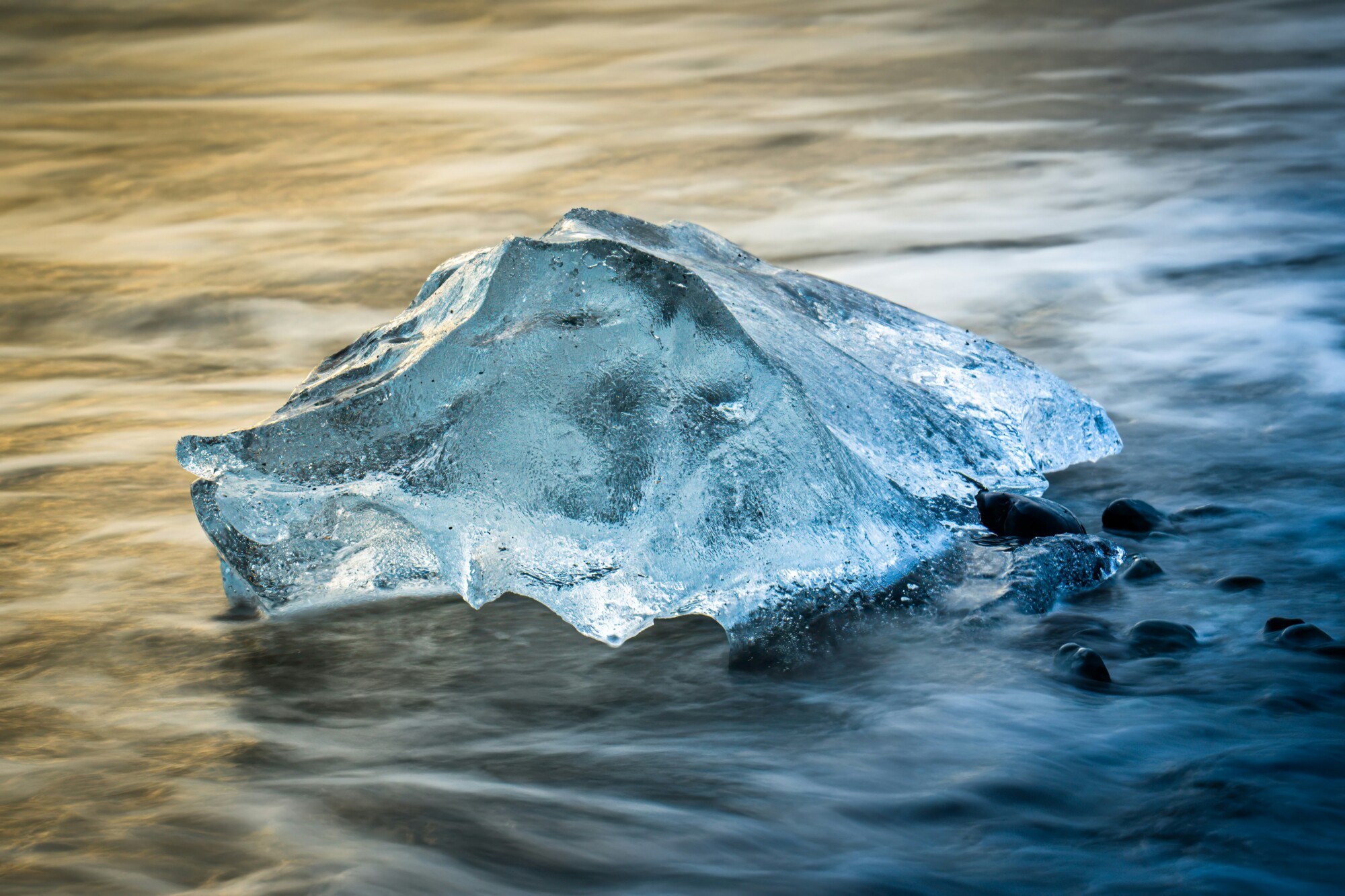 Glasklarer Eisbrocken liegt im fließenden Wasser eines Flusses oder Sees, umgeben von sanften Wellen.