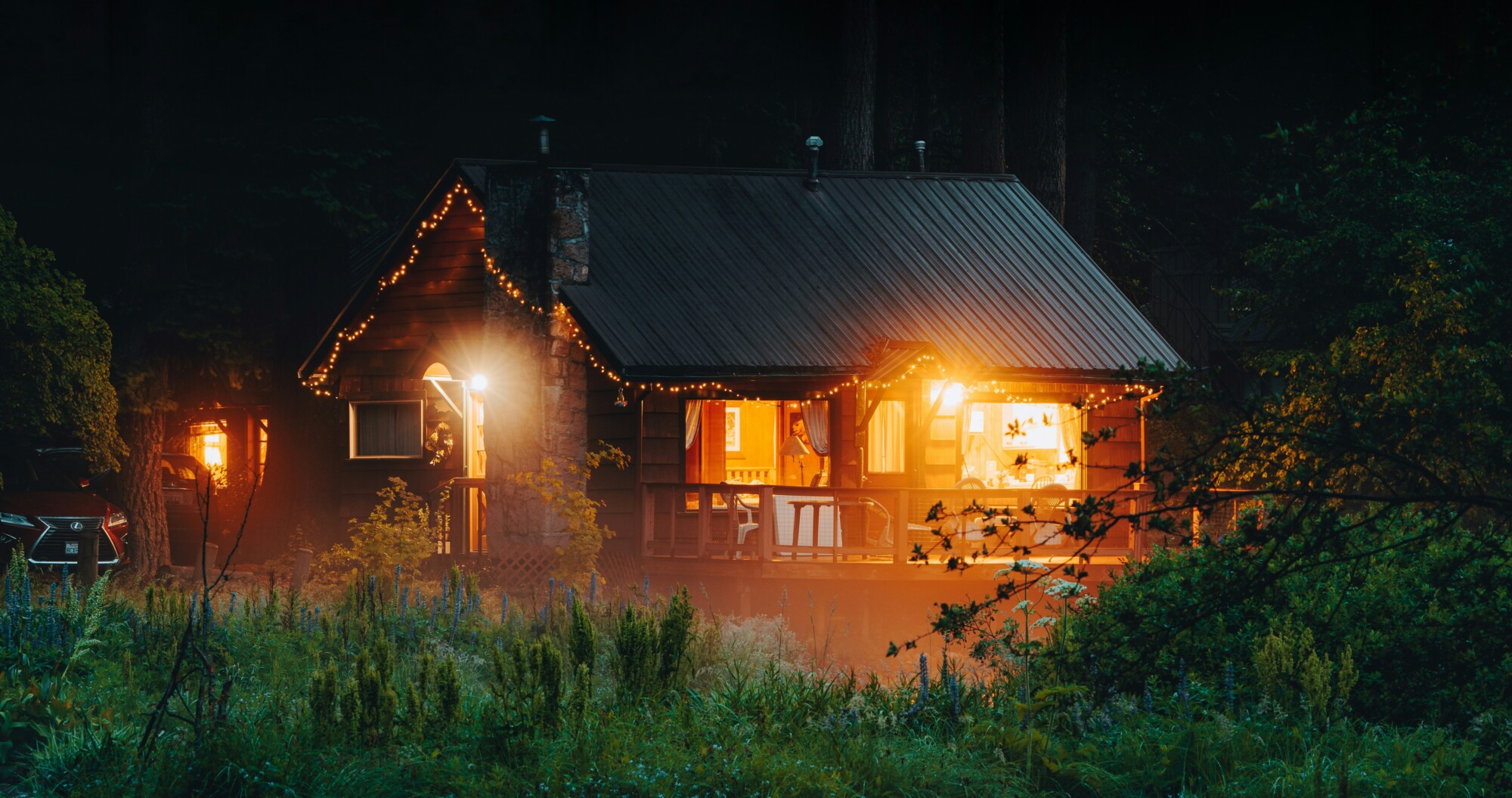 Gemütliche Hütte mit warmem Licht steht am Ufer eines Flusses inmitten eines Waldes.