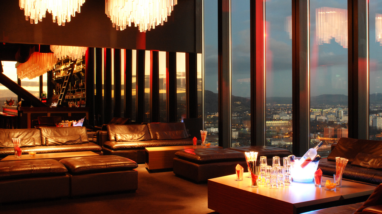 Bar Lounge Location Basel Die Bar ist ein vielseitiger Ort, der eine Bar, Lounge und Veranstaltungsbereich kombiniert. Sie bietet ein passendes Ambiente für verschiedene Firmenveranstaltungen. Nutzen Sie die Gelegenheit, das Team bei einem entspannten Afterwork-Drink zu stärken, Ihre Kunden mit einem leckeren Apéro riche zu beeindrucken oder die exklusive Location für Seminare und Präsentationen zu nutzen. Die Aussicht über das lebendige Stadtleben von Basel verleiht jedem Anlass eine besondere Note und macht ihn unvergesslich. Erleben Sie die Location selbst und lassen Sie sich von ihr begeistern.