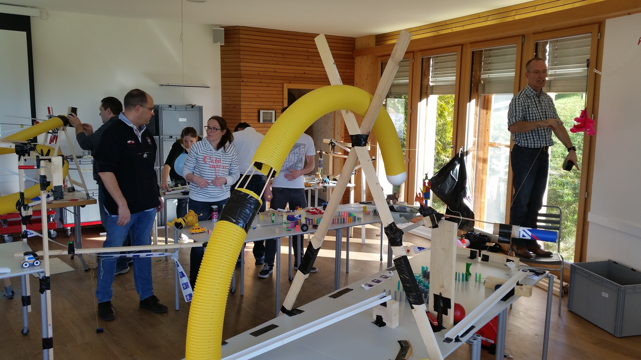 Kettenreaktion PLUS So kreativ sind Ihre Mitarbeitenden! Jeweils vier Personen bauen an einem Tisch aus unterschiedlichsten Materialien einen Abschnitt der Kettenreaktion. Dabei können auch Ihre Produkte integriert werden. Anschliessend werden mit den angrenzenden Teams die Schnittstellen besprochen und gebaut. So entsteht eine riesige Kettenreaktionsmaschine.
