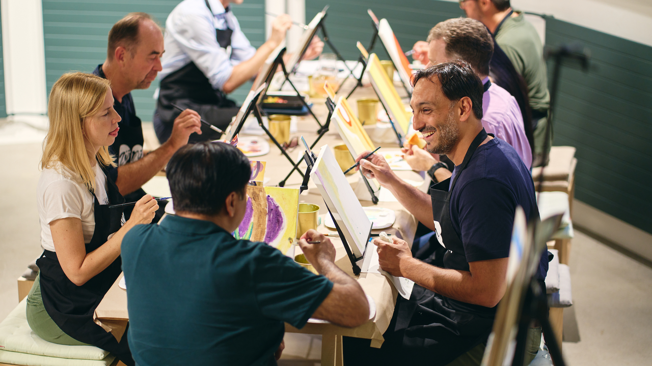 Gemeinsam malen Teamevent Pinsel, Farbe, Staffelei und ein professioneller Künstler – wir kommen mit allem, was man für einen Malevent braucht, in die Location eurer Wahl. Gemeinsam malen wir, was euch als Team zusammenschweisst – ein Porträt oder auch viele kleine Bilder, die zukünftig eine Wand in eurem Büro dekorieren. So sieht kreatives Team-Building aus.