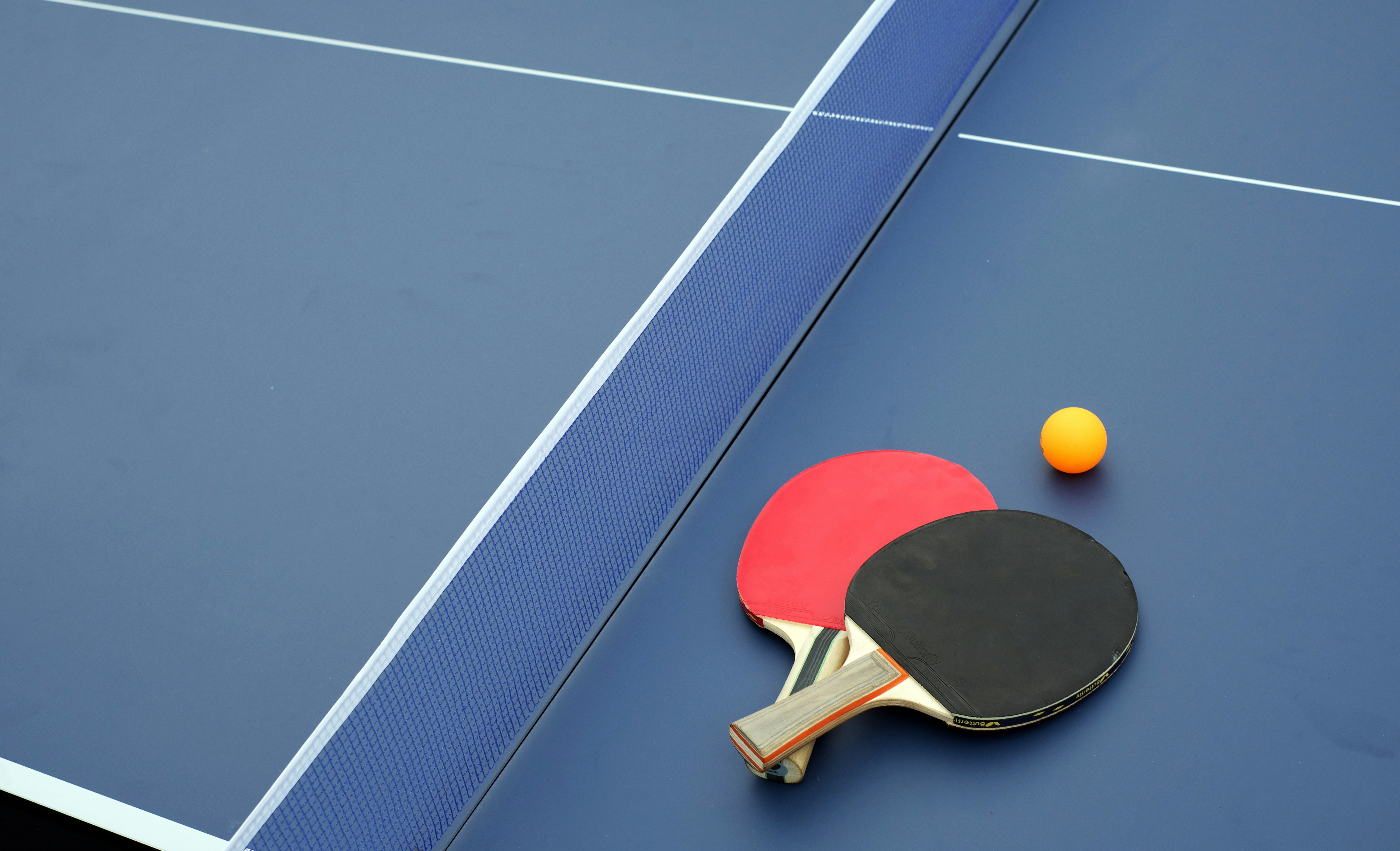 Auf dem Bild ist ein Teil eines Tischtennistisches zu sehen. Auf dem Tisch liegt ein Tischtennisschläger und ein Tischtennisball.
