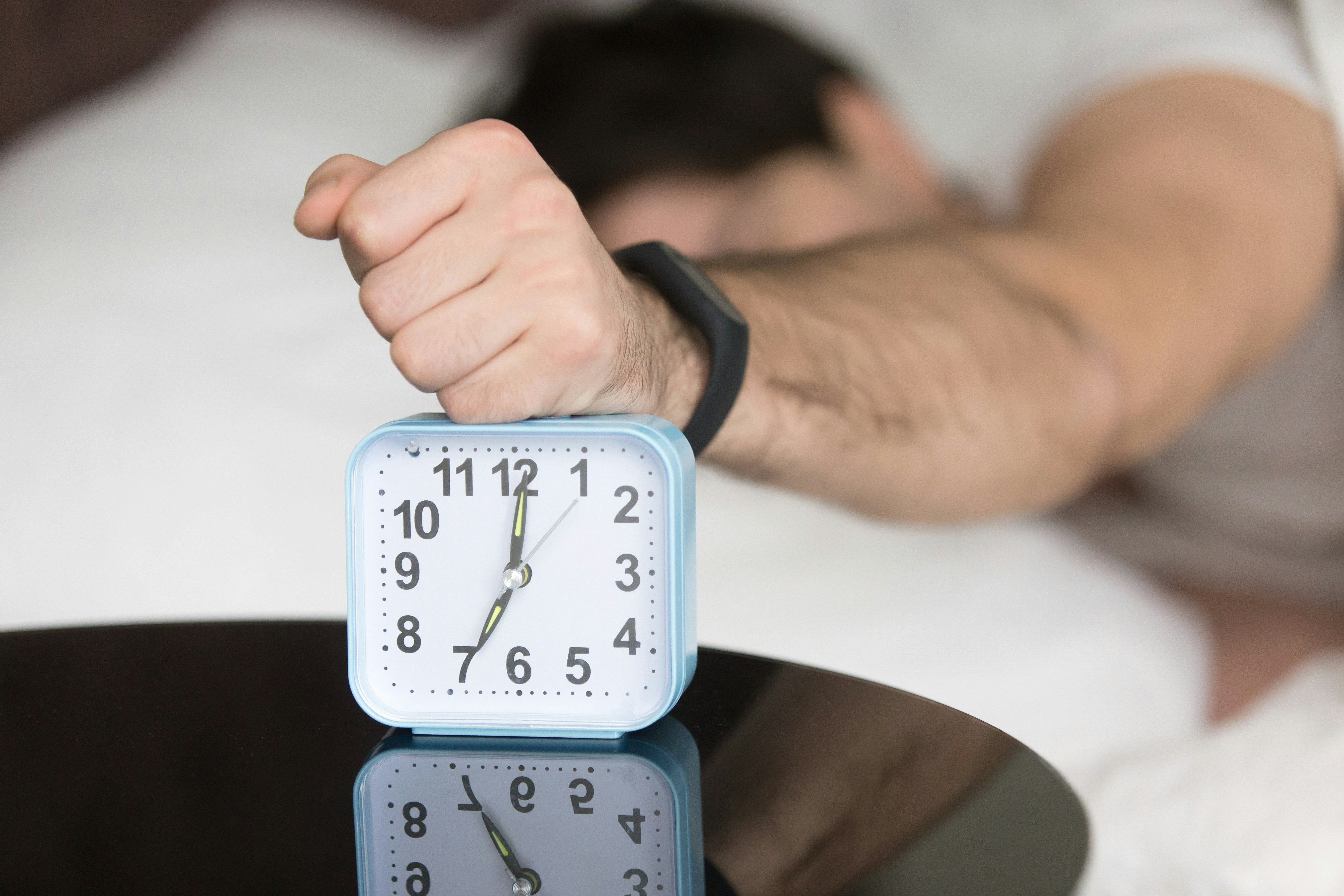 Ein Mann haut aus dem Bett auf seinen Wecker